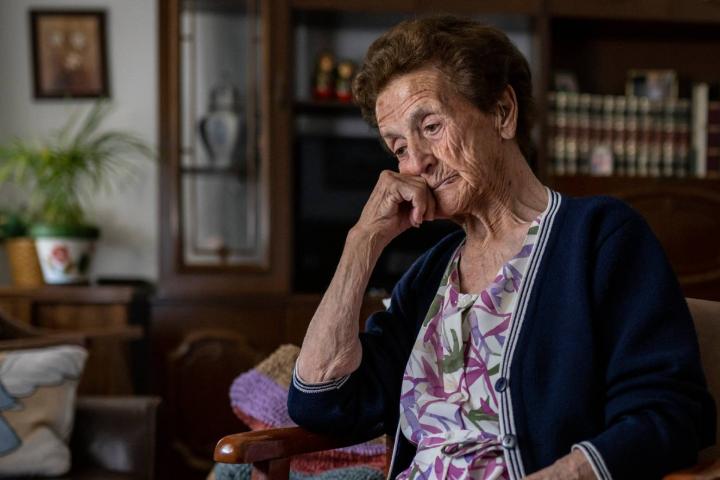 Mujer mayor sentada sola en el sofá, con gesto triste, pensando en sus problemas, recordando momentos de su vida, echando de menos a sus hijos y sintiendo soledad