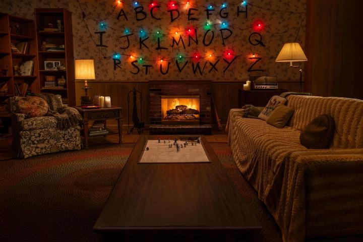 Salón de los Byers de Stranger Things con la pared del alfabeto iluminada y la chimenea encendida.