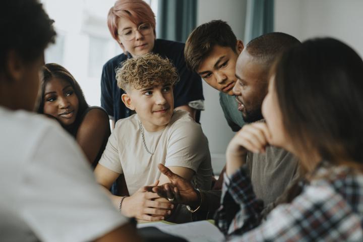Chicos y chicas adolescentes con una persona no binaria escuchando a un profesor discutiendo en el aula - Fotografía de stock