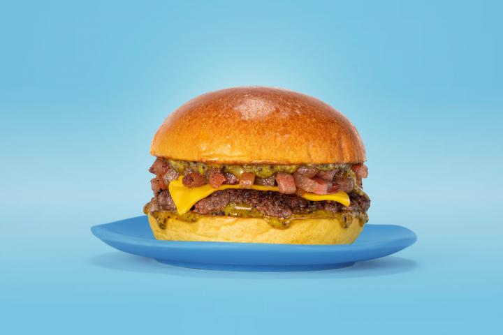 Hamburguesa con queso cheddar derretido, trocitos de bacon y salsa verde sobre un pan brioche en un plato azul