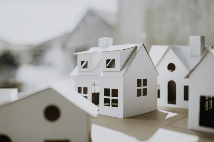 Imagen conceptual y sencilla de casas de cartón, blancas, lisas, de diversas formas y tamaños, con espacio para copiar.