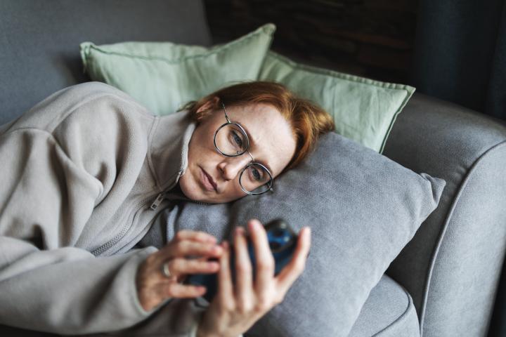 Mujer adulta tumbada en la cama con el móvil, triste y deprimida, malas noticias