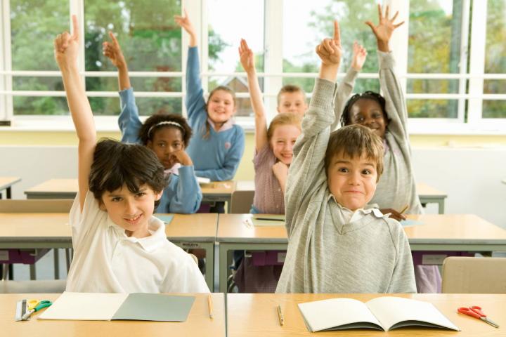 Niños levantan la mano enmedio de clase y tenemos a un pillo entre ellos
