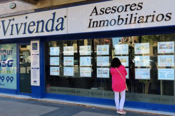 Mujer mirando anuncios de venta y alquiler en el escaparate de una inmobiliaria.