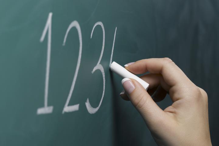 Una profesora escribiendo números en la pizarra.