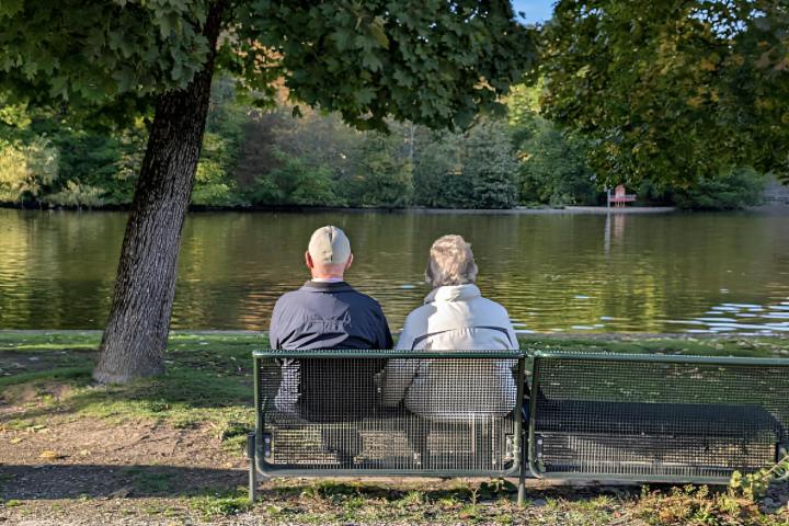 Una pareja de jubilados sentados de espalda de cara a un lago