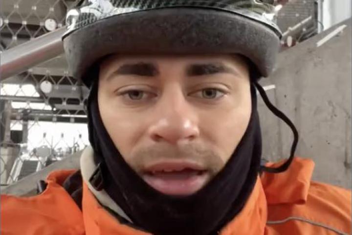 Repartidor español de Just Eat en Suiza, con casco y chaqueta naranja, grabándose en vídeo para explicar su salario y condiciones de trabajo.