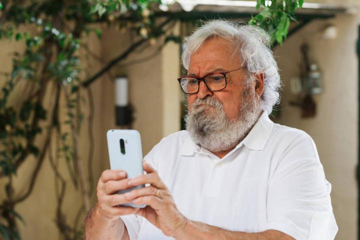 Hombre mayor confundido usando un teléfono móvil al aire libre
