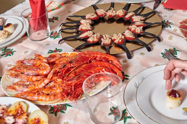 Plato de camarones a la plancha y plato de aperitivos sobre una mesa con mantel con motivos navideños. preparación de la cena navideña familiar.