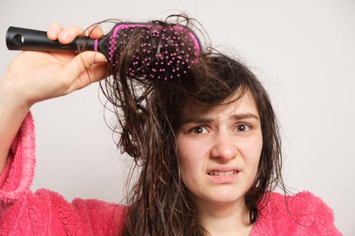 Una mujer trata de peinarse el pelo mojado y enredado. Cuidado del cabello en casa, pérdida de cabello y sección