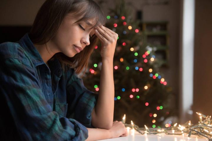 Mujer con dolor de cabeza junto a un árbol de Navidad