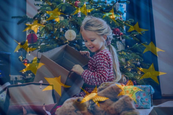 Una niña descubre sus regalos de Navidad bajo el árbol, rodeada de estrellas de la bandera de la UE.
