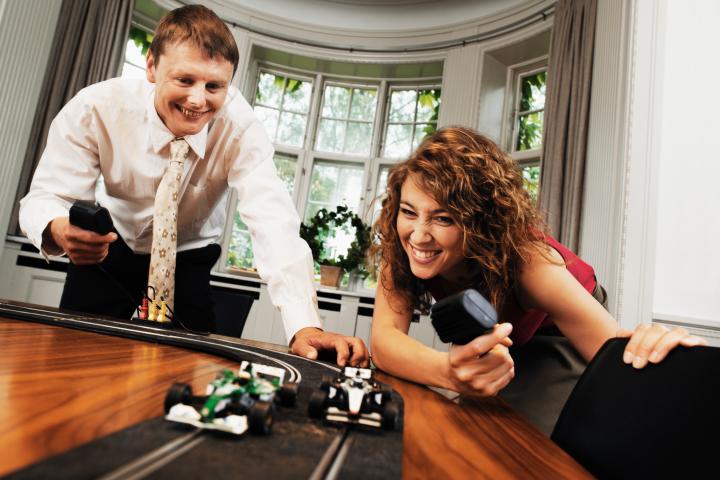 Imagen de dos personas adultas, jugando con el Scalextrix, sin que nadie repare en que no hay niños en la habitación.