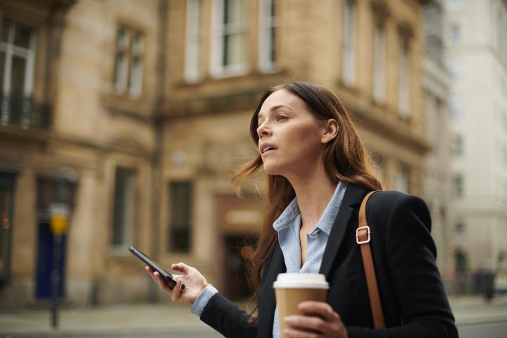 Imagen de una mujer dirigiéndose al trabajo, con un café en la mano.