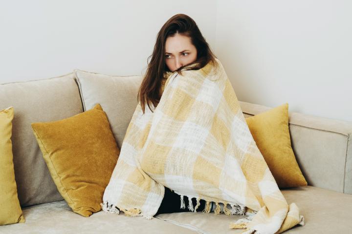 Una mujer protegiéndose del frío en su casa con una manta.