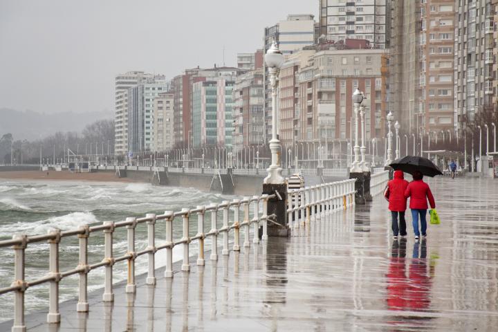 Una pareja anda por la calle bajo la lluvia en un día frío de invierno en Gijón (Asturias)