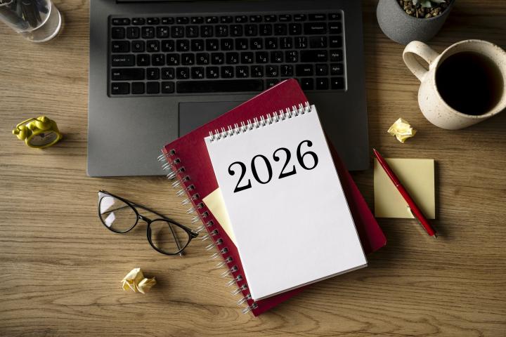 Bloc de notas con el texto "2026" sobre un escritorio de madera. Planeando propósitos para el Año Nuevo 2026. Portátil, gafas y bolígrafo.