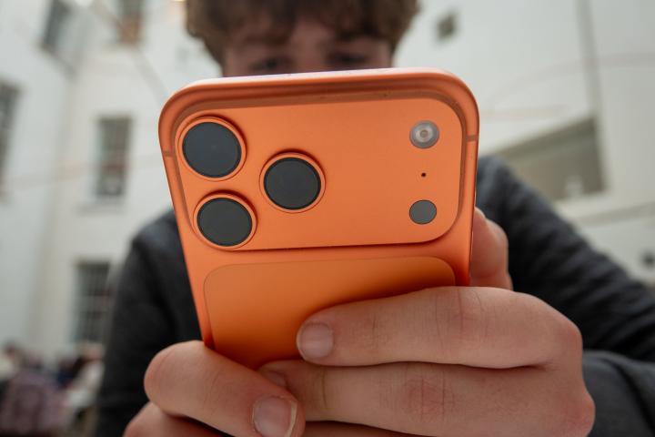 Una fotografía en primer plano de un adolescente sosteniendo un smartphone con funda naranja y un sistema de triple cámara.