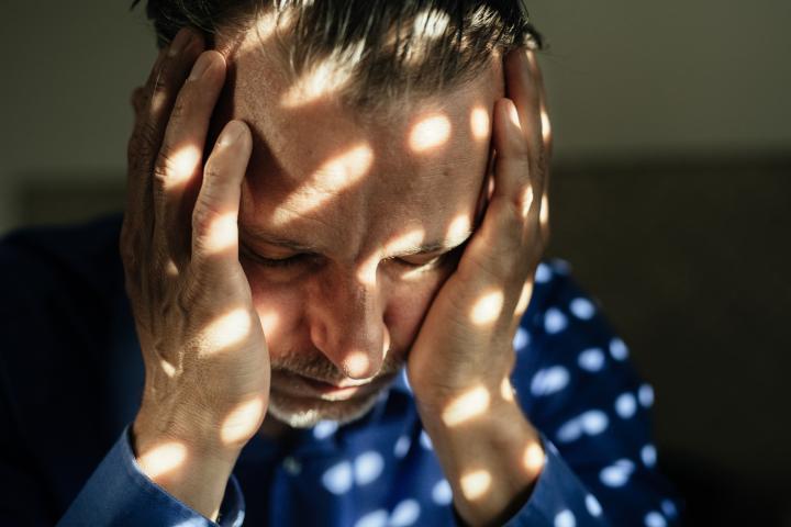 Hombre maduro deprimido sentado en una habitación oscura con algunos reflejos del sol