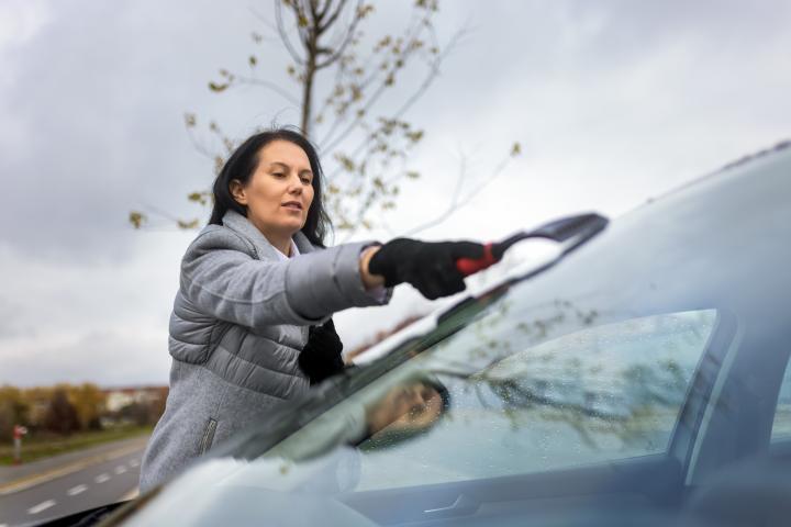 Una mujer intentando quitar el hielo de su coche.