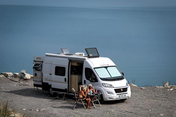 Dos viajeros se sientan fuera de su autocaravana estacionada en la orilla un lago