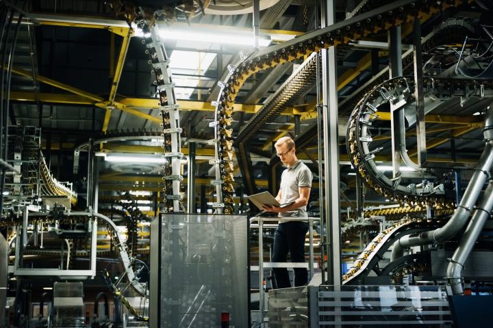 Ingeniero sosteniendo una computadora portátil en una fábrica entre máquinas y transportadores