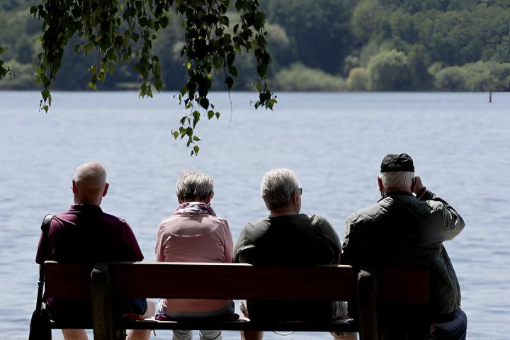 Un grupo de personas mayores sentadas en un banco frente a un lago