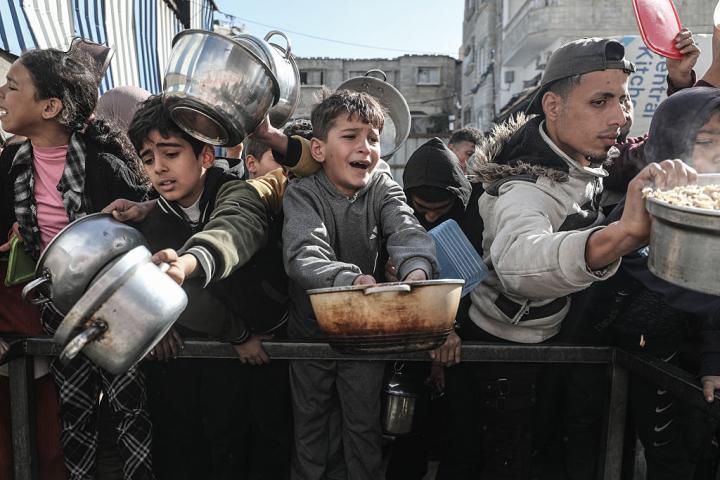 Ciudadanos de Gaza tratan de lograr una comida caliente, distribuida por organizaciones benéficas, en el campo de refugiados de Nuseirat, el 12 de enero de 2026.