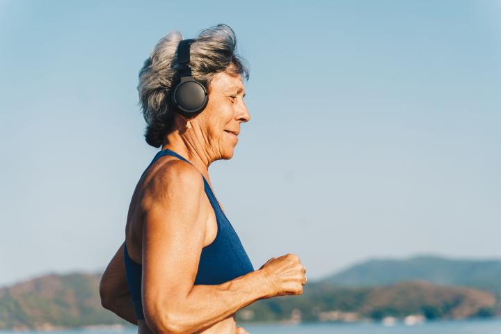 Mujer mayor con auriculares corriendo por el terraplén, día soleado de verano.
