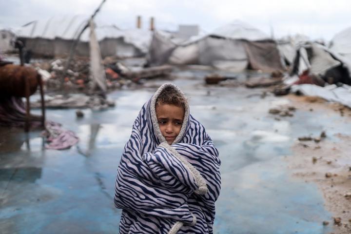 Una niña se protege del frío frente a la tienda de campaña de su familia, dañada por una tormenta, en un campamento de desplazados en Gaza ciudad, el 13 de enero de 2026.