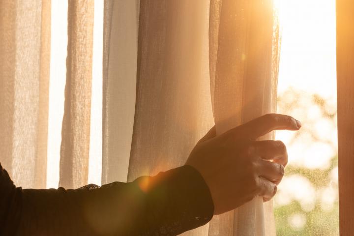 alt="alt="La mano de una mujer abre las cortinas blancas de la ventana del dormitorio. Por la mañana, miró la vista de las montañas y los árboles. Admira la naturaleza junto con la frescura -""