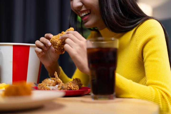 Feliz joven asiática comiendo delicioso pollo frito en casa