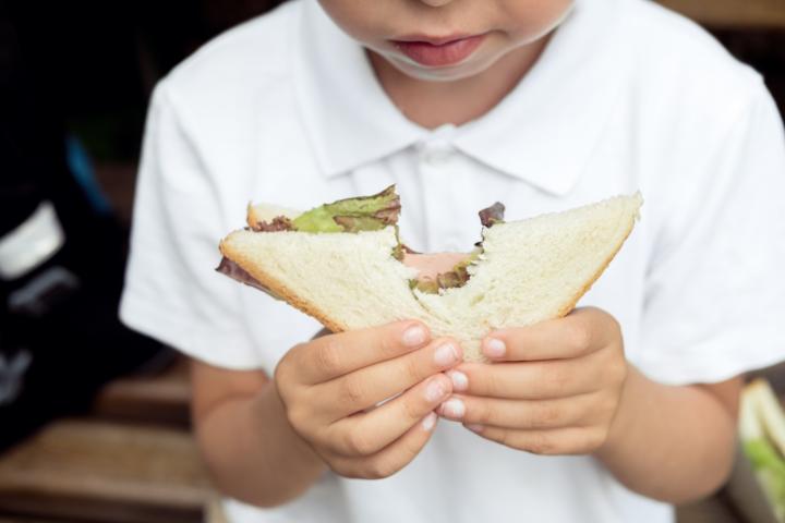 Un estudiante con polo blanco y gafas mordiendo su sándwich en el recreo