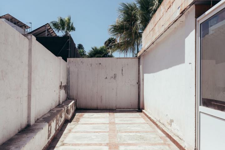 Muro de bloques y chapa metálica que cierra el acceso a una vivienda unifamiliar, impidiendo la salida directa a la calle.