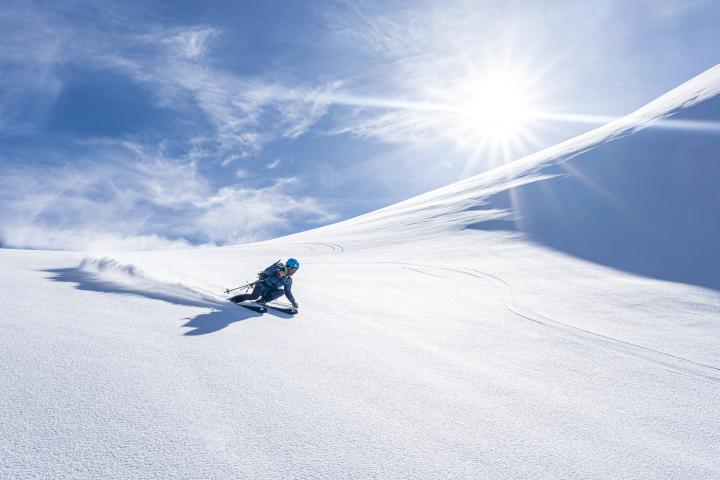 alt="alt="Man powder skiing on a steep snowy mountain ridge on a bright winter day, Valais Canton, Switzerland""