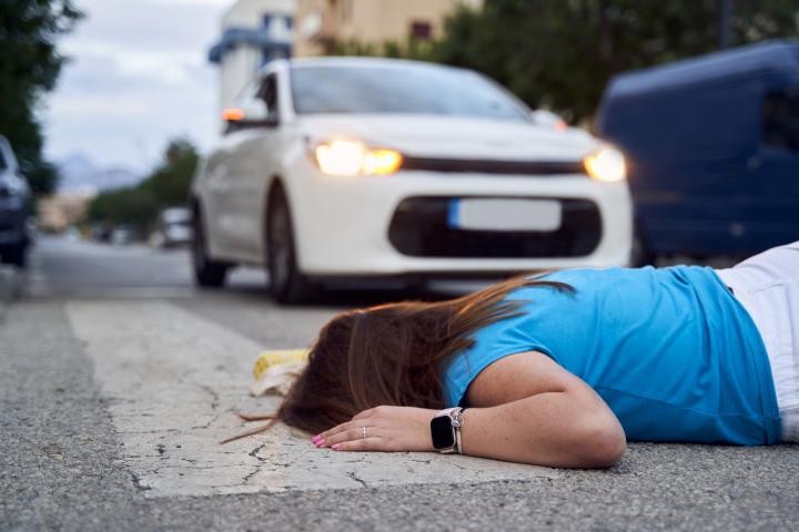 Side view of an unrecognizable young woman lying on the ground at a crosswalk after being hit by a car. Concept of hit-and-run and traffic accidents in the city.