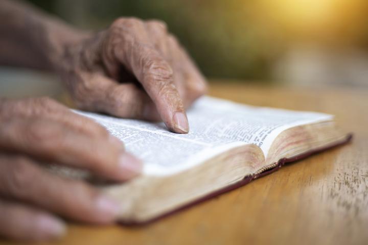 alt="alt="Un anciano leyendo su Biblia mientras está sentado afuera.""