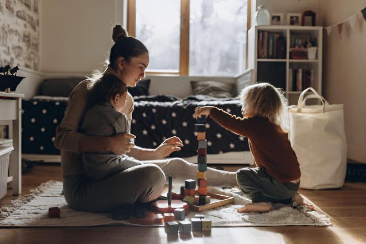 Una madre joven jugando con niños mientras está sentada en el suelo de casa