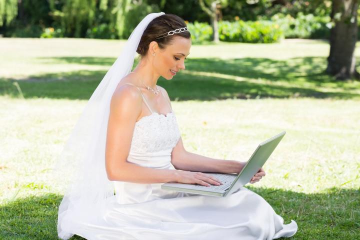 Una novia usando una computadora portátil mientras está sentada en el césped del jardín