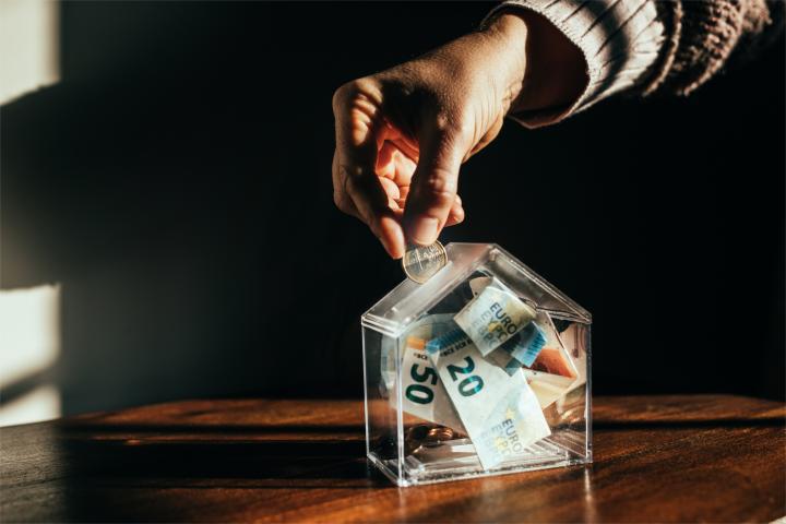 Una persona introduciendo una moneda en una hucha con forma de casa
