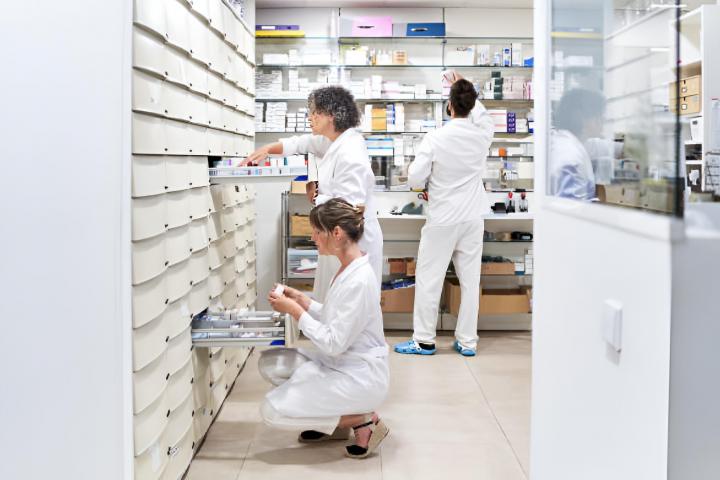 Tres miembros del personal buscan un medicamento en un cajón de una farmacia