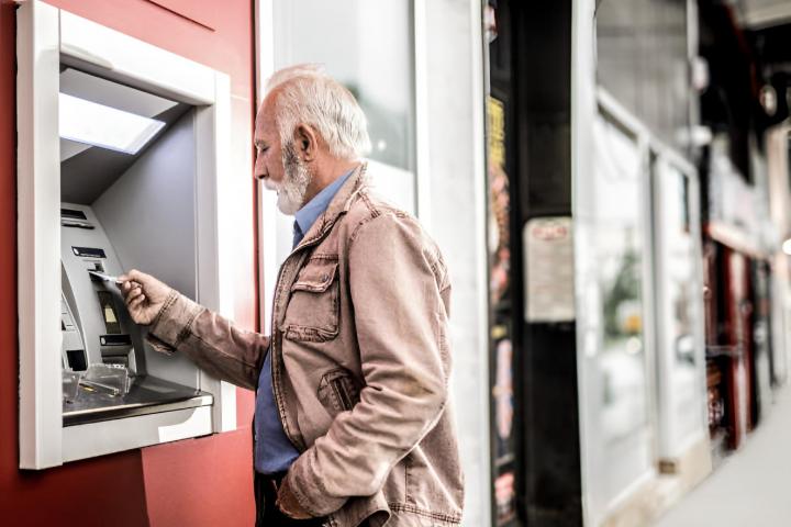 Un hombre mayor insertando una tarjeta de crédito en cajero automático