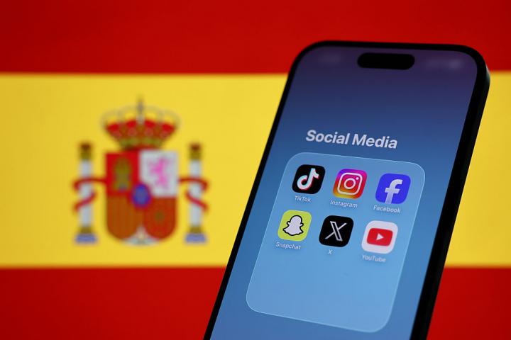 Un teléfono con varias aplicaciones de redes sociales, sobre una bandera de España, ante el debate presentado por el presidente, Pedro Sánchez, y los menores de edad.