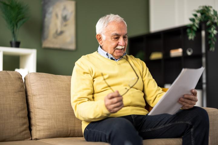 Hombre mayor sentado en el sofá y leyendo su plan financiero
