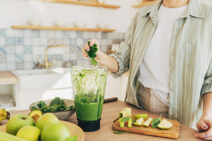 Joven preparando un batido verde saludable en la cocina