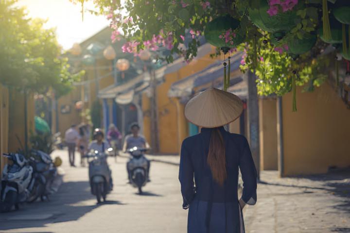 Una mujer vietnamita con ropa tradicional y sombrero cónico visitando el casco antiguo de Hoi An en Vietnam