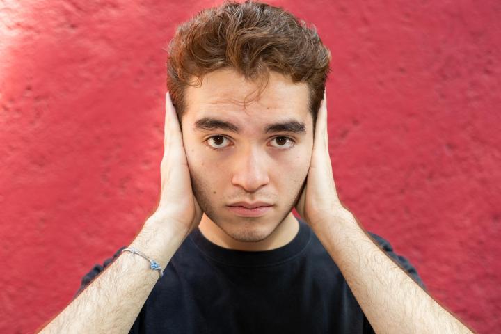 Joven mirando a la cámara y tapándose los oídos.