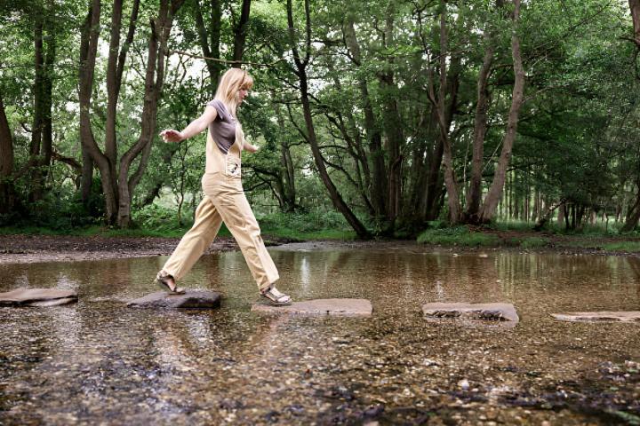 Una mujer joven caminando sobre rocas en el río