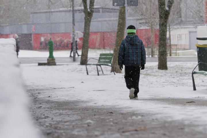 Vista trasera de un niño con ropa de invierno caminando por las calles de la ciudad en un día nevado.