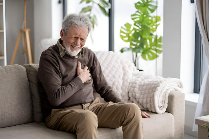 Un anciano sosteniendo su mano sobre su corazón con una una mueca de dolor